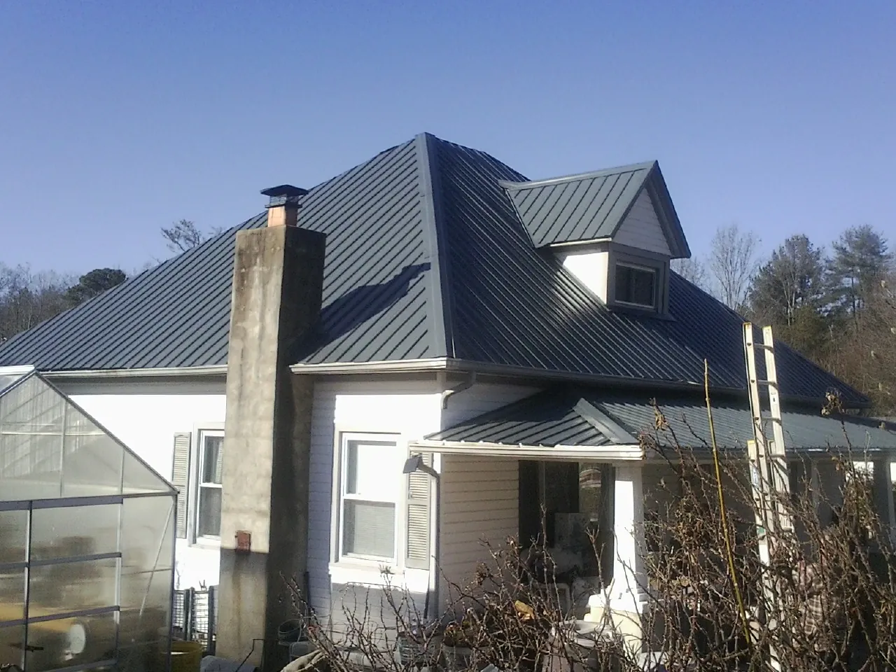 Dark blue standing seam metal roof on a white farmhouse with dormer — Slate & Tile Roof Repair by Roofing Brothers in Midland