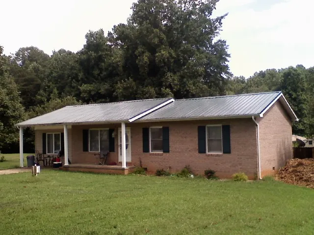 Gray metal roof on a brick ranch house with a side carport in Midland