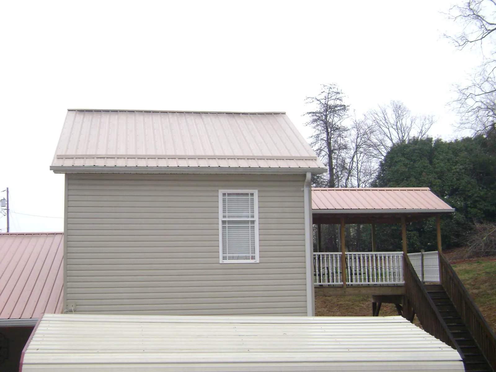 Tan metal roofs on a two story addition and attached porch, from a Roof Replacement job in Midland